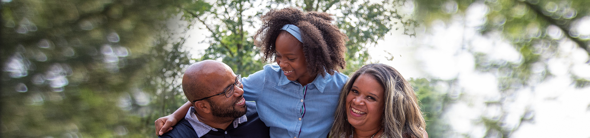  black family with mom, dad, and young daughter outside smiling 